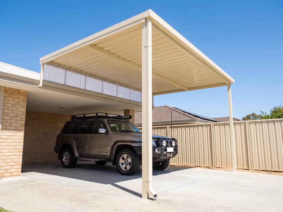 A raised flat carport lifted above the eave, its single roof plane sloping to the outer posts