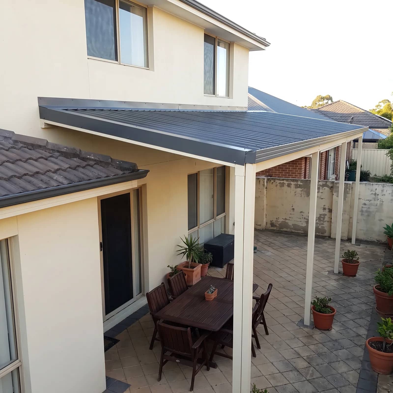 A raised flat patio attached to a Perth home, its single roof plane sloping down from above the house gutter to the front posts