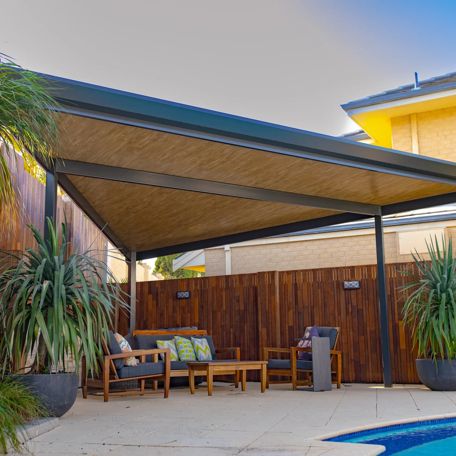 A flat roof patio over a poolside alfresco in Perth, with a timber-lined underside and dark steel posts
