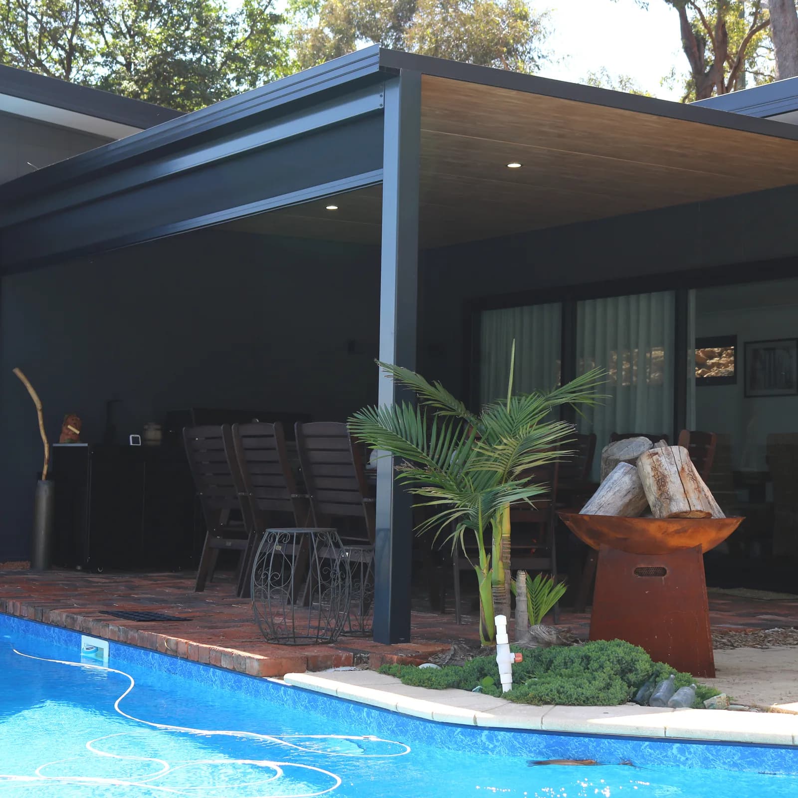 A flat roof patio in dark Colorbond over a paved pool surround, with downlights in the underside