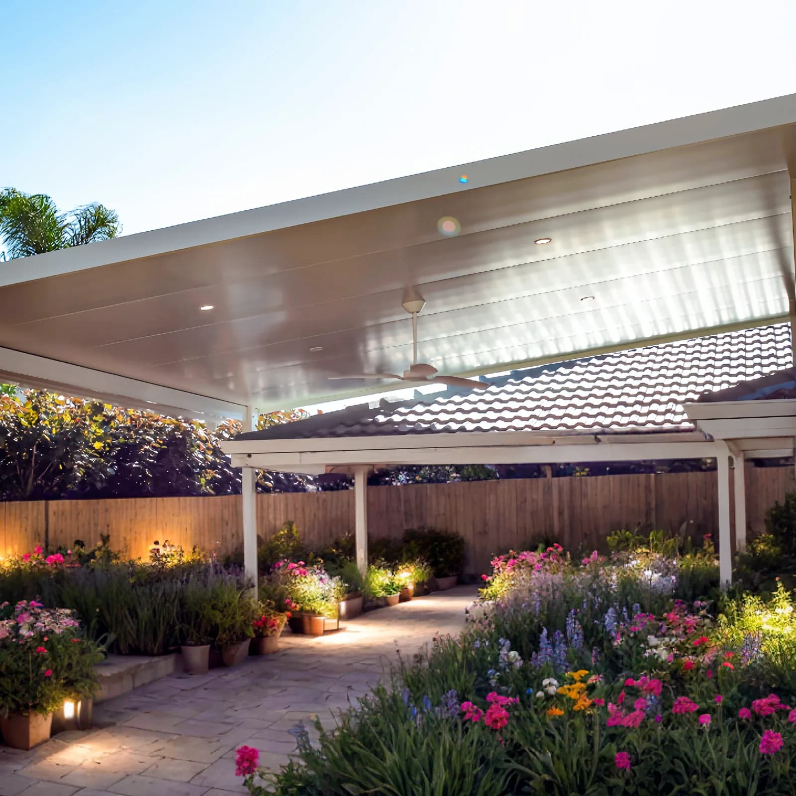 A flat roof patio running the length of a Perth home at dusk, garden lighting picking out the beds along the edge