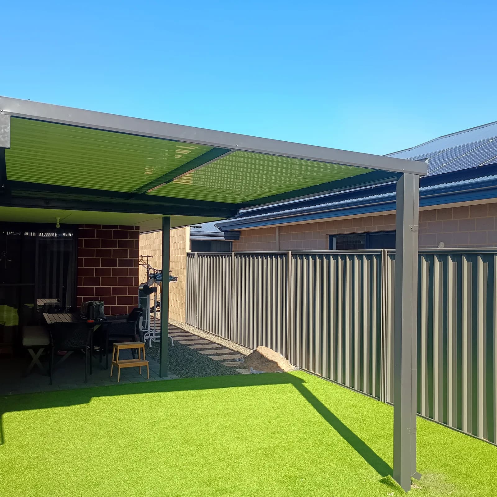 A flat roof patio in dark Colorbond over artificial lawn, attached along a brick wall