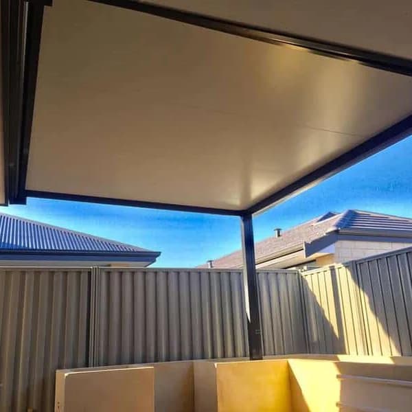 Looking up at an insulated patio roof from underneath, its panels meeting a dark boundary fence