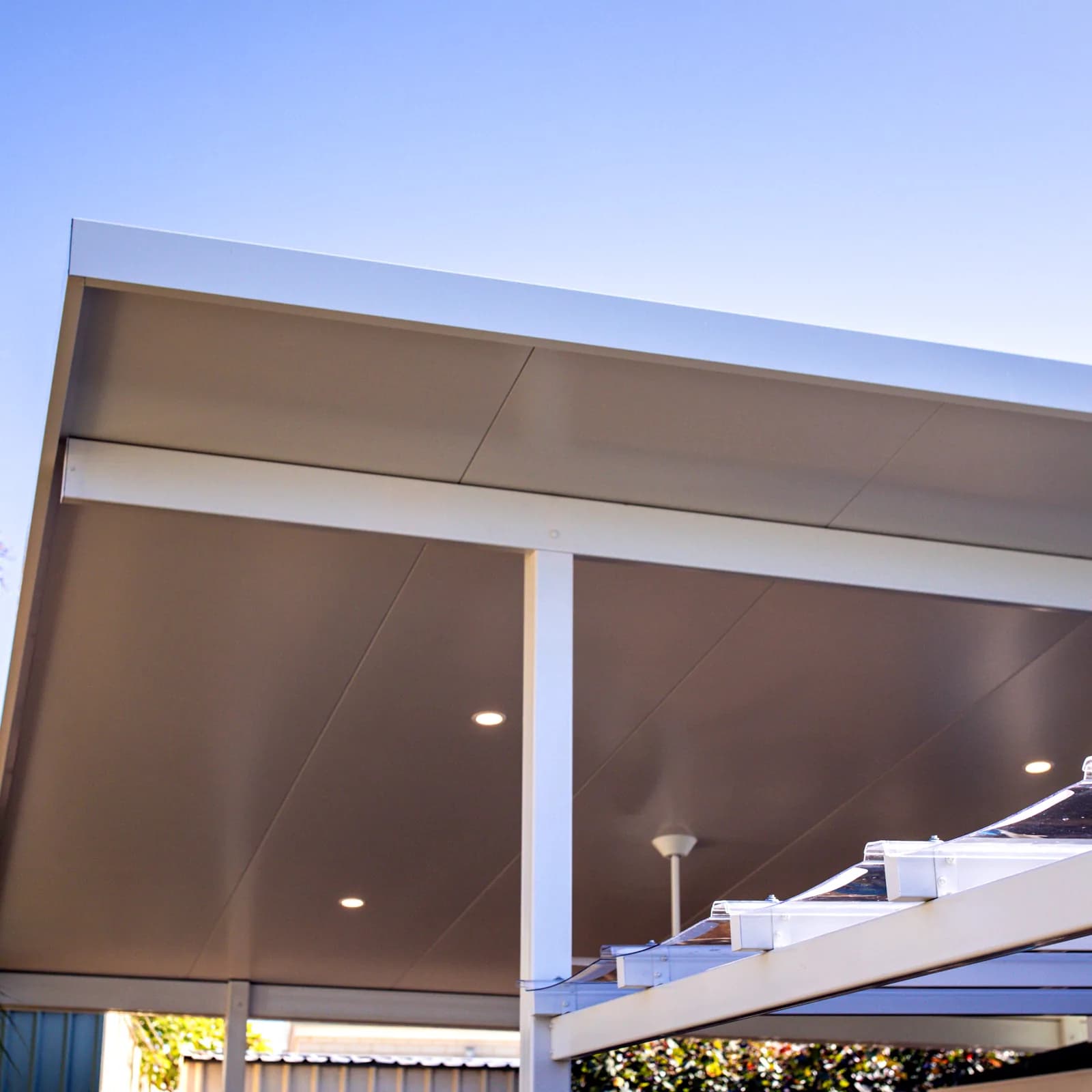 The underside of an insulated patio roof, showing the flat lined ceiling and recessed downlights